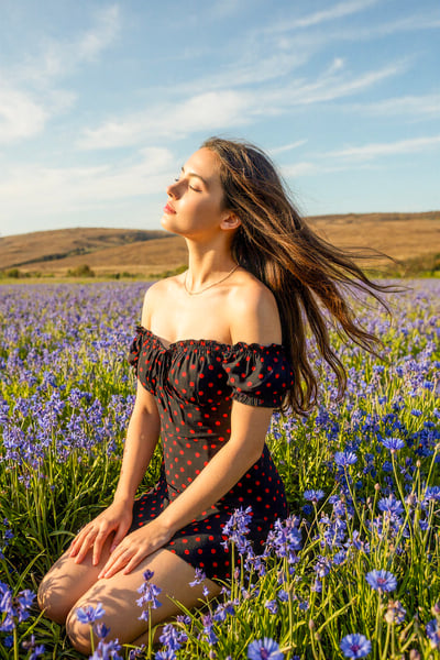 Young Woman Kneeling in a Windy Blue Wildflower Field (Natural Sunlight Portrait) thumbnail